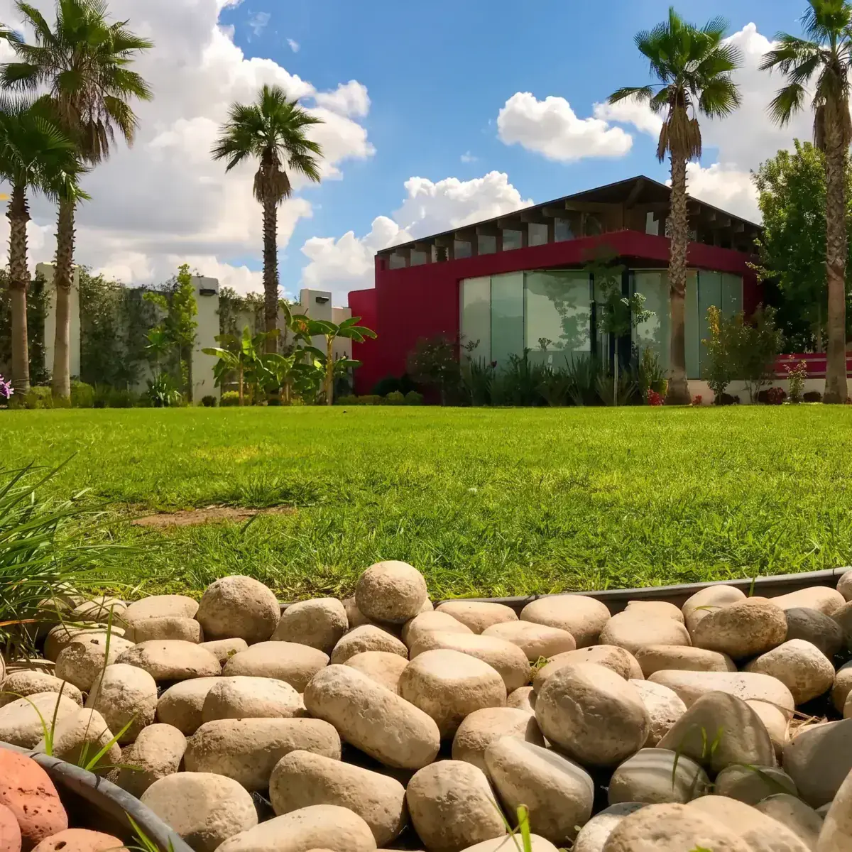 Jardines de Hacienda de Samotracia con césped, palmeras y edificio principal con fachada roja y ventanales.
